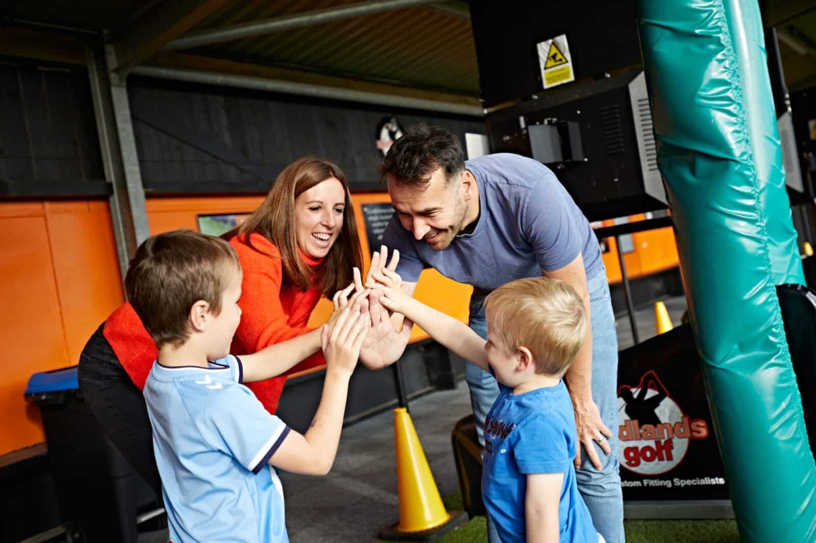 A family of 4 with 2 adults and 2 young boys enjoying spending time together learning to play golf