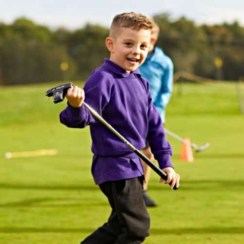 Junior Boys Golf - A young boy in a purple jumper is holding his junior golf club.
