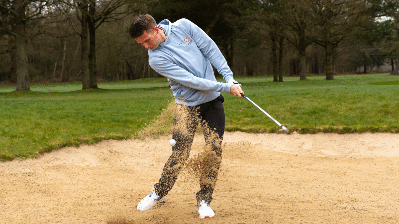 Golfer mid-swing getting a ball out of the bunker