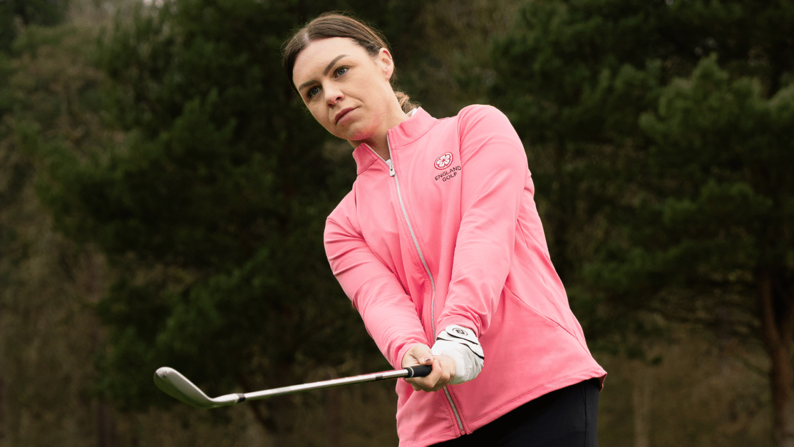 Female golfer mid-swing focusing on their shot