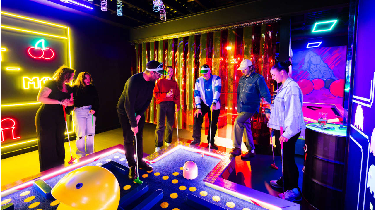 Group of friends playing neon mini golf in an arcade-style glow-in-the-dark venue.